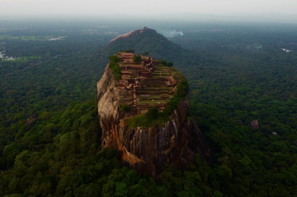 A stunning aerial view of Sigiriya Rock Fortress rising above lush greenery in Sri Lanka.