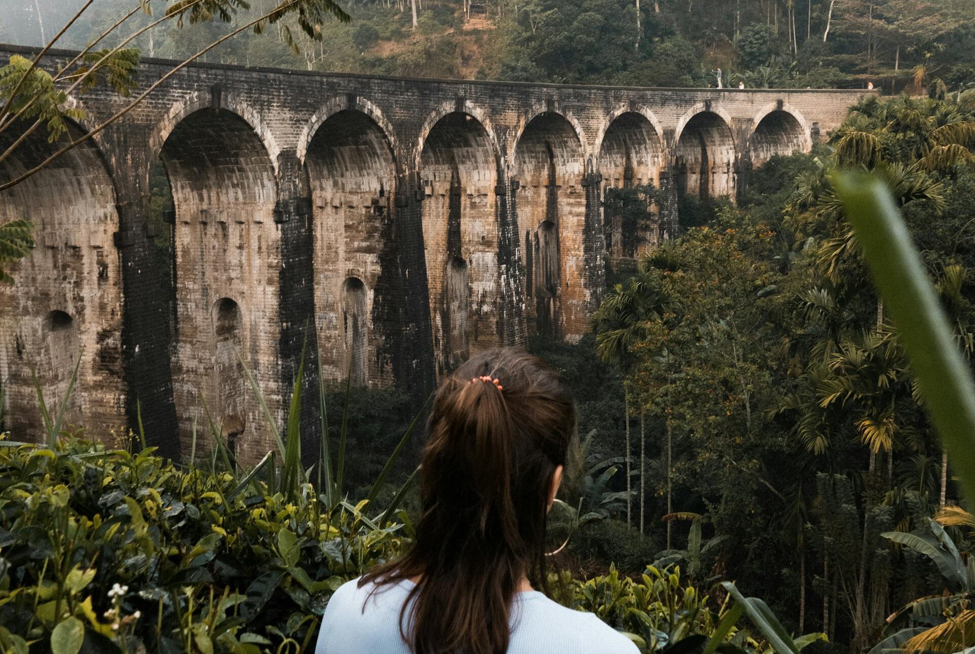 Explore the lush jungle surrounding the iconic Nine Arches Bridge in Ella, Sri Lanka, with a serene back view of a woman.